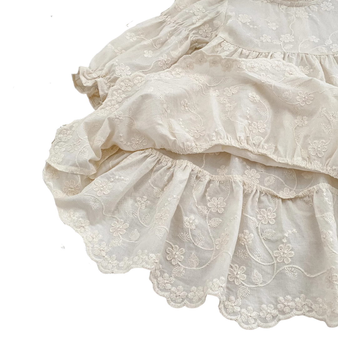 Detailed close-up of the tiered ruffle skirt and scalloped hem on the girls ivory floral embroidered dress.