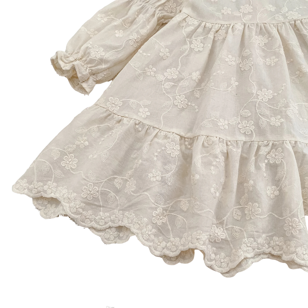 Angled view of girls ivory floral embroidered dress showcasing tiered skirt and long bishop sleeves.