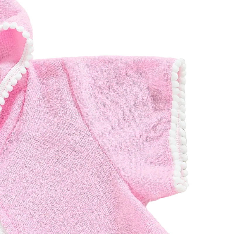 Close-up of the short sleeve on a pink terry cloth swim cover-up featuring white pom-pom trim detail.