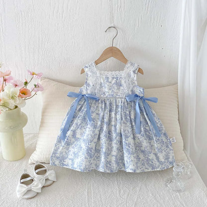 Blue and white Toile de Jouy print girls dress hanging against a white background with decorative shoes.