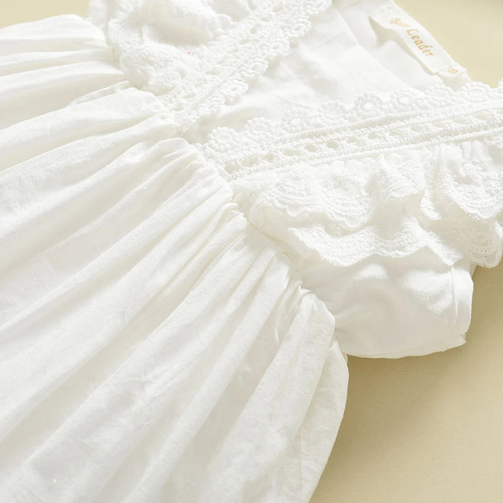 Close-up detail of the intricate floral lace overlay and pleating on the bodice of the girls white cotton dress.