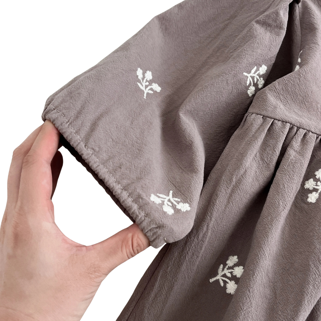 A hand gently stretching the gathered elastic sleeve cuff of the gray floral girls dress to show flexibility.