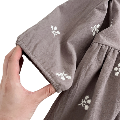 A hand gently stretching the gathered elastic sleeve cuff of the gray floral girls dress to show flexibility.