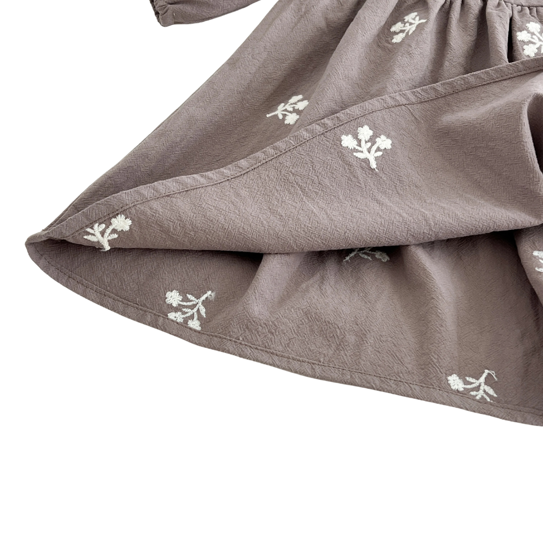 Close-up of the gently waving skirt hem on the gray cotton girls dress showing the delicate white floral embroidery.