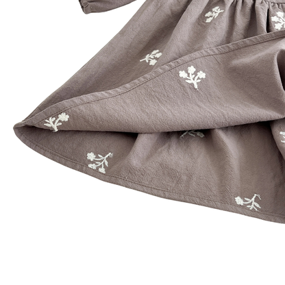 Close-up of the gently waving skirt hem on the gray cotton girls dress showing the delicate white floral embroidery.