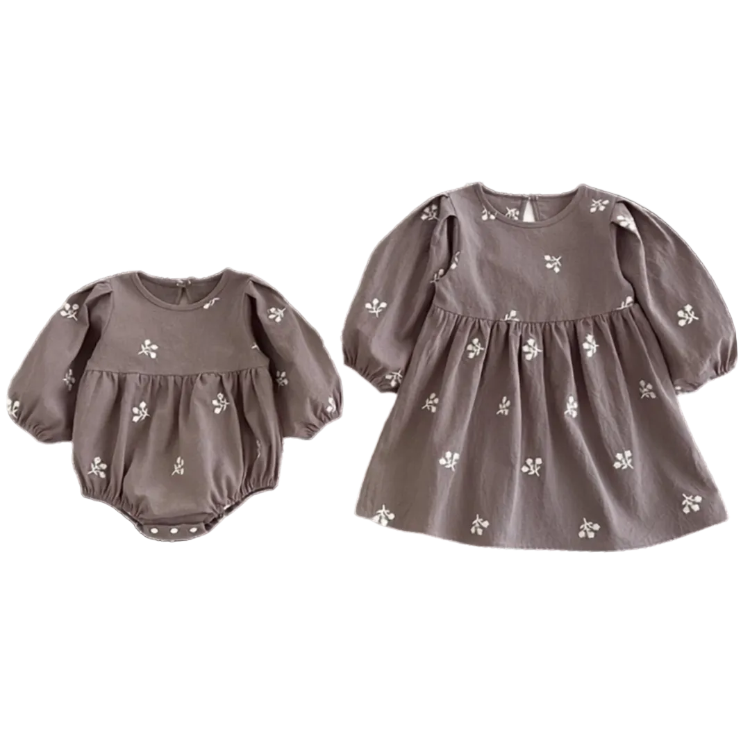Flat lay displaying the grey baby romper next to the matching older sister long-sleeve floral dress.