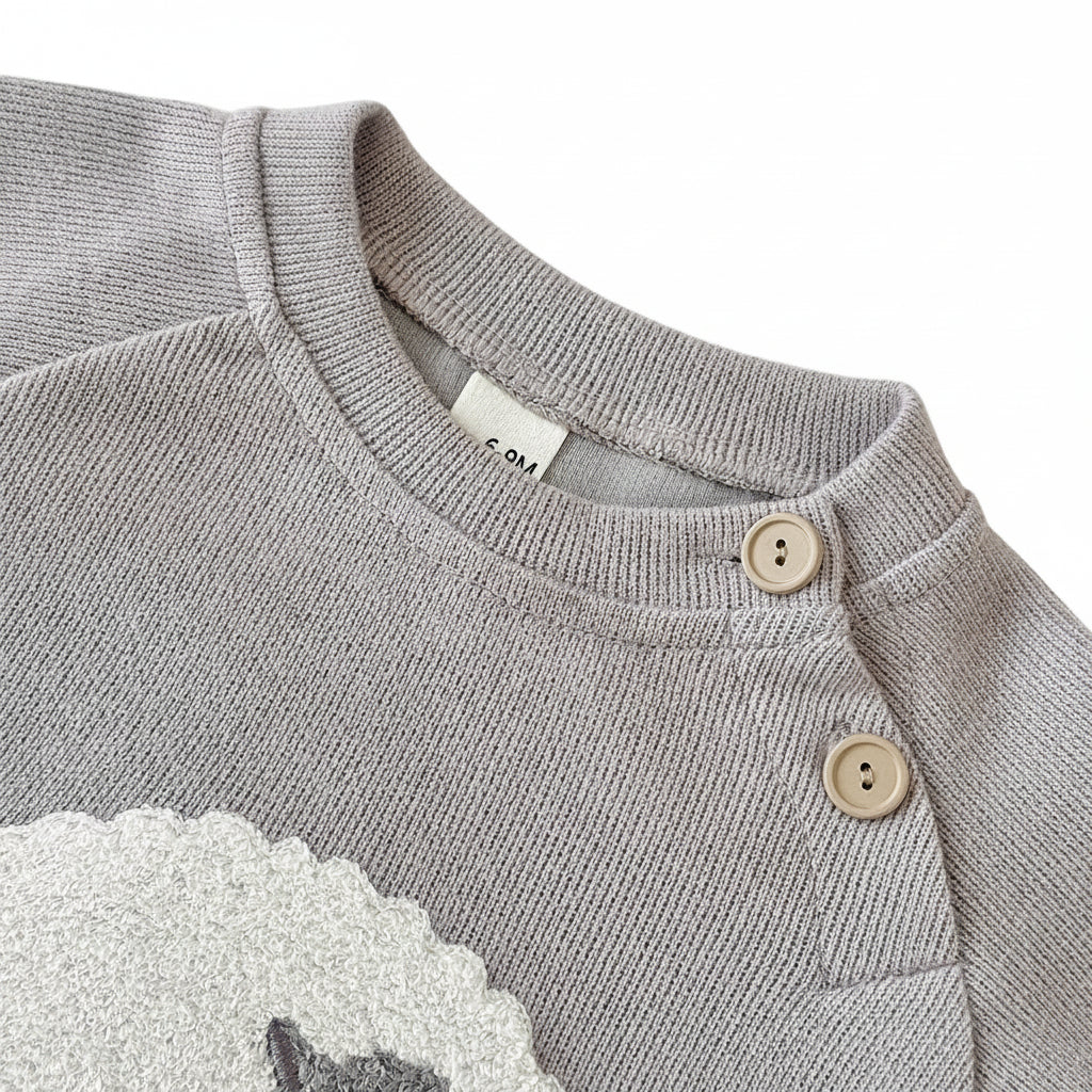 Close-up of the grey knit baby sweater detailing the ribbed neckline and two wooden shoulder buttons for easy dressing.