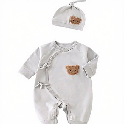 Front view of the grey long-sleeve baby sleepsuit with side snaps and matching teddy bear patch hat.