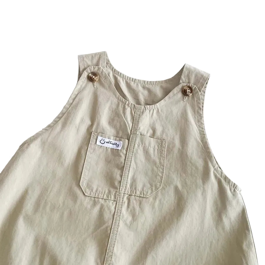 Detailed view of the front chest pocket and wooden-style buttons on the Hamptons Beige baby boy dungarees.