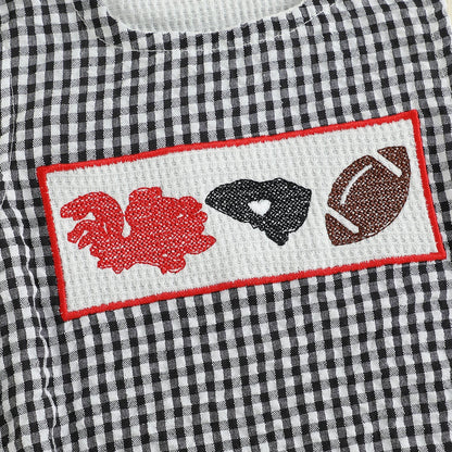 Micro detail of the hand-smocked chest panel on the baby romper, displaying an embroidered red rooster character design, black state map outline, and a classic brown football.