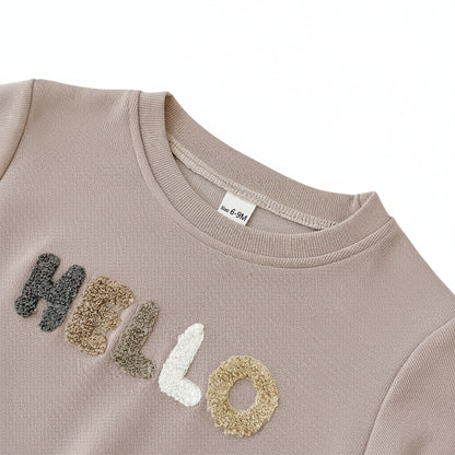 Close-up of the textured towel letter embroidery spelling HELLO on the chest of the beige baby sweatshirt.