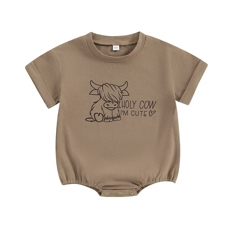 lat lay of a light brown short-sleeve baby romper featuring a Highland cow graphic and the text "HOLY COW I'M CUTE".