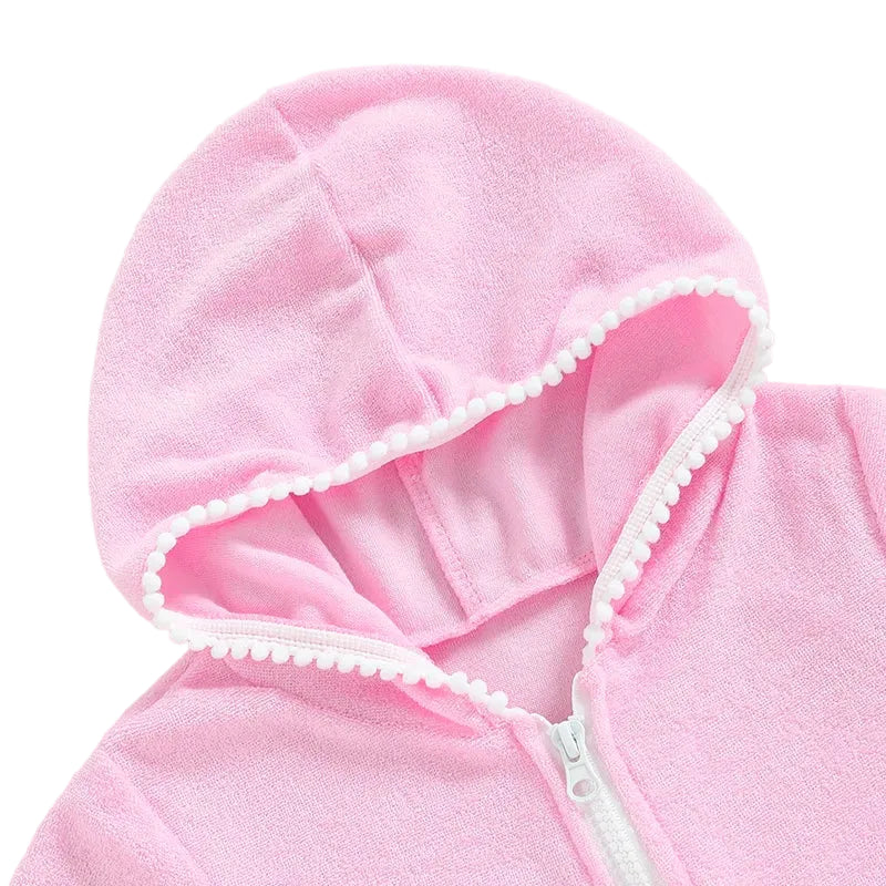 Detailed view of the hood and white zipper on a pink girls' terry cloth beach dress with decorative pom-pom edging.
