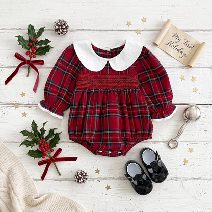 Infant baby girl red plaid smocked Christmas bubble romper styled with white Peter Pan collar, holiday props, and black shoes