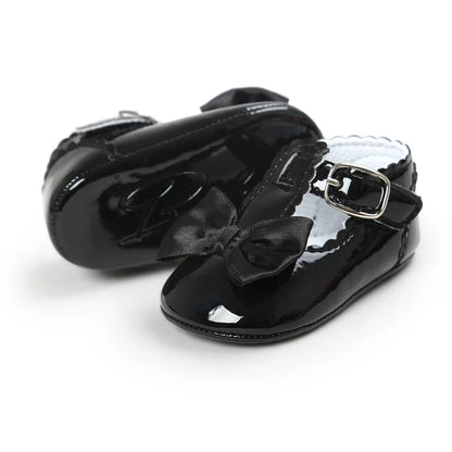 Side and back view of infant black patent leather T-strap Mary Janes showcasing the scalloped trim collar and durable outsole.