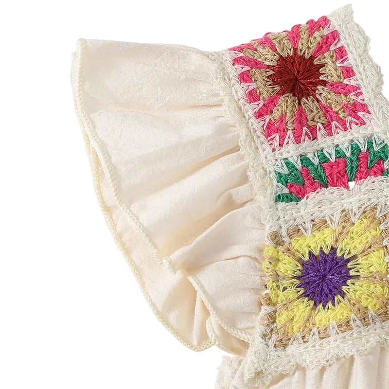Extreme close-up of the textured cream cotton fabric and ruffled fly sleeve detailing on the baby girl romper.