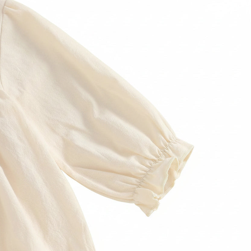 Detailed close-up view of the loose, comfortable fabric and soft elasticized ruffle wrist cuff on the long-sleeve baby romper.