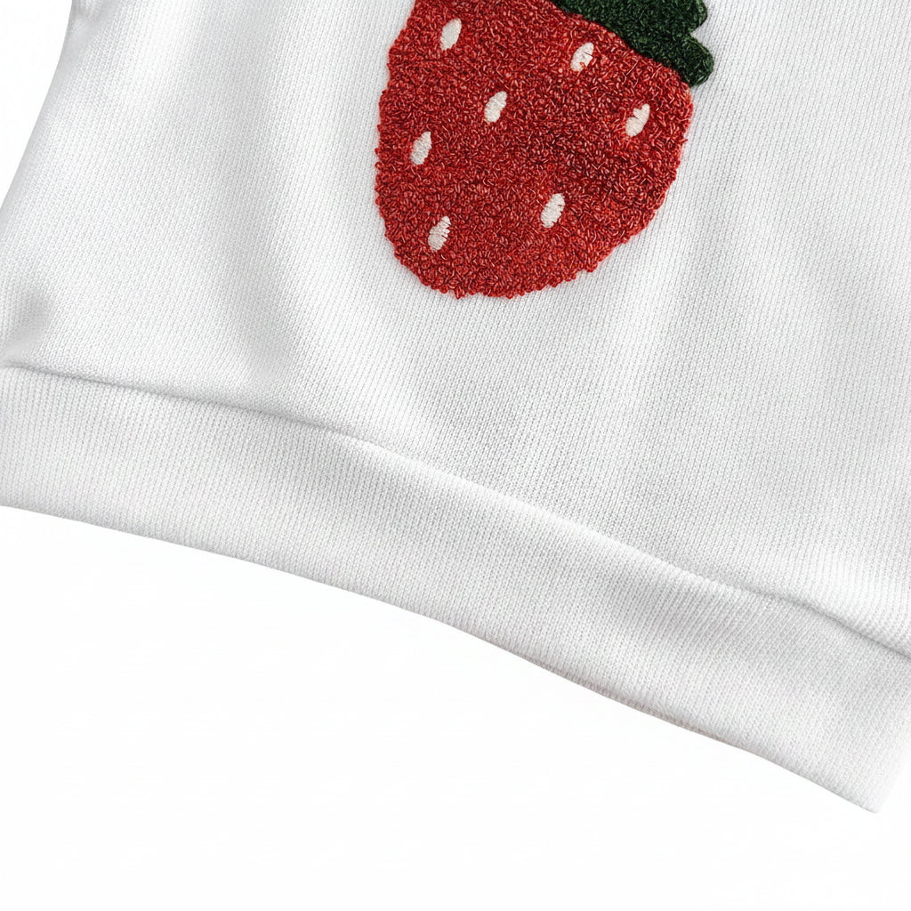 Detailed close-up of the premium combed cotton weave, elastic bottom hem, and stitched edge of the baby pullover with the bottom of the strawberry applique.