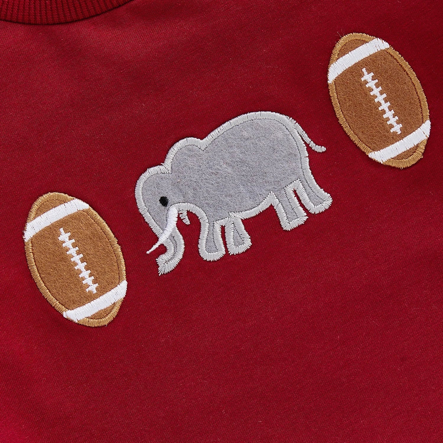 Close-up of high-quality vintage chain-stitch embroidery featuring a grey elephant and classic footballs on a crimson infant romper.