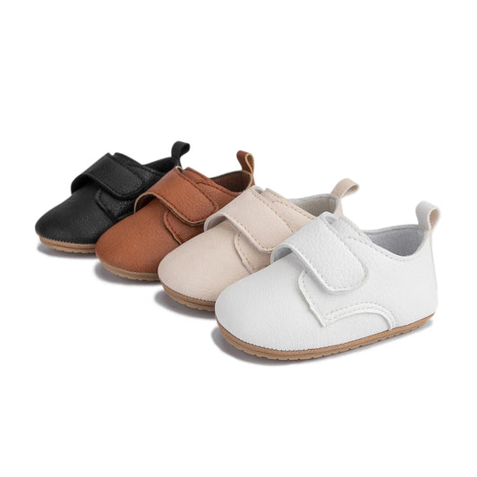Four pairs of infant first walker faux leather shoes lined up in black, brown, beige, and white.