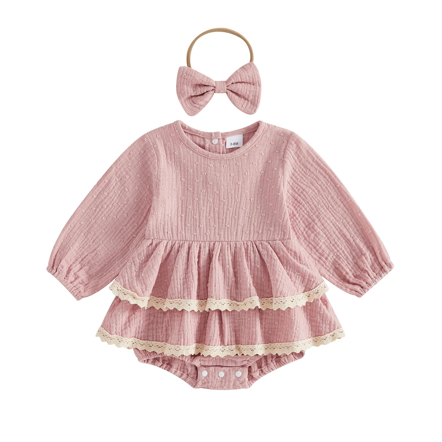 Flat lay of a vintage-inspired dusty pink infant girl puff sleeve romper dress with lace trim and matching bow headband.