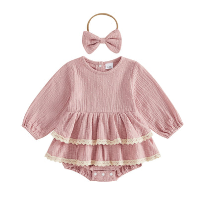 Flat lay of a vintage-inspired dusty pink infant girl puff sleeve romper dress with lace trim and matching bow headband.