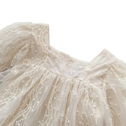 Close-up of the square neckline and intricate bodice embroidery on an infant girl ivory lace romper.