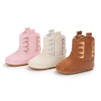 A lineup of three infant metallic western boots on a white background, showcasing the available color options: pink, white with silver details, and cognac brown with gold details.