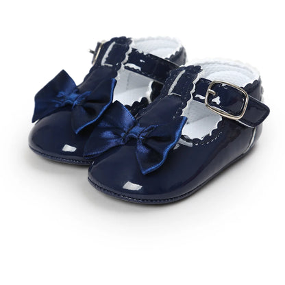 Front angled view of infant navy blue patent leather dress shoes highlighting the secure strap fastener and scalloped collar trim.