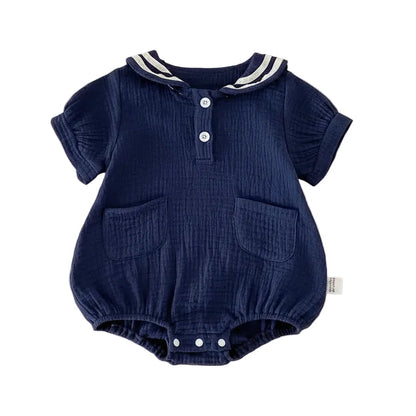 Flat lay of a Deep Sea navy blue muslin baby bubble romper with white nautical stripes on the sailor collar and a relaxed unisex fit.