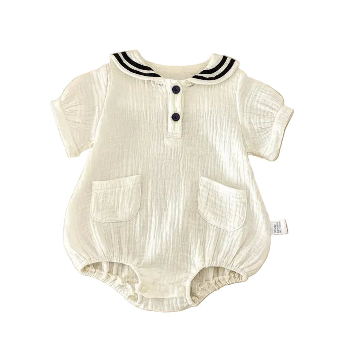 Flat lay of an off-white Sea Salt muslin baby romper with a navy nautical collar, showing the natural crinkle texture of the cotton fabric