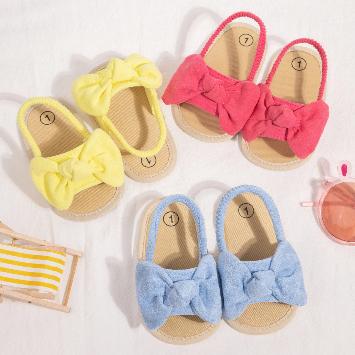 Flat lay of baby girl soft sole bow sandals showing all three available summer colors: yellow, blue, and pink.