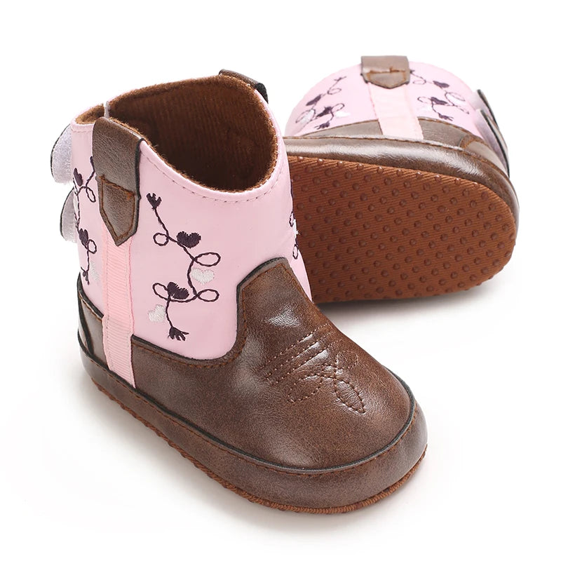 Angled view of a pair of pink baby girl western boots showing the soft non-slip sole construction.