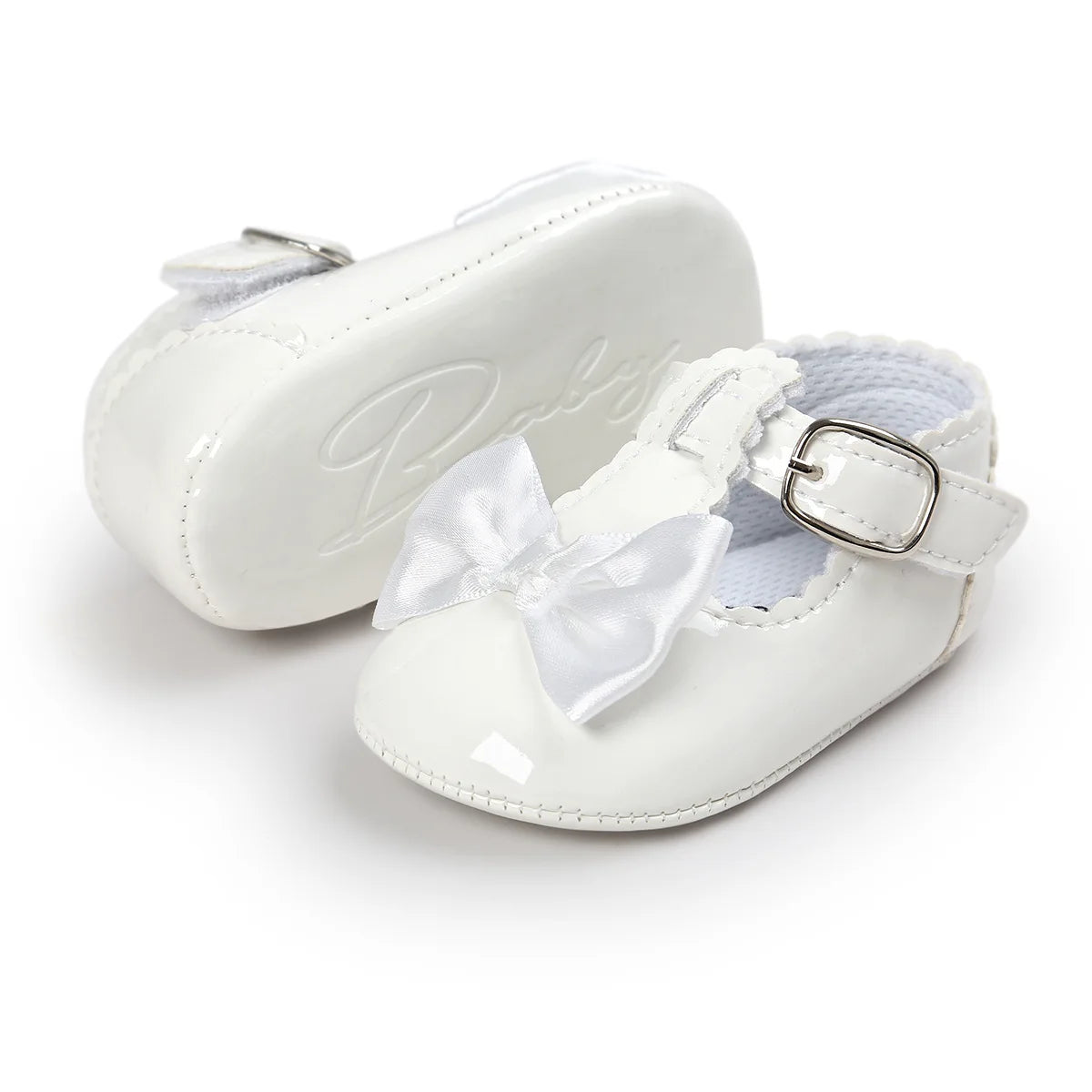 White patent leather infant dress shoes showing the side profile strap and the bottom rubber sole with an embossed cursive design.