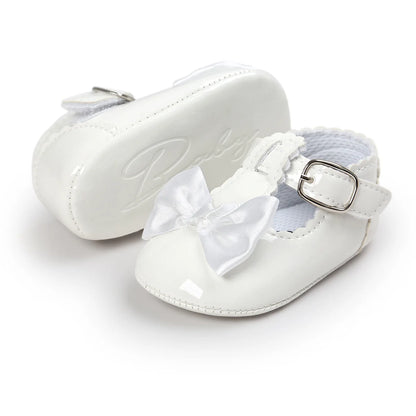 White patent leather infant dress shoes showing the side profile strap and the bottom rubber sole with an embossed cursive design.