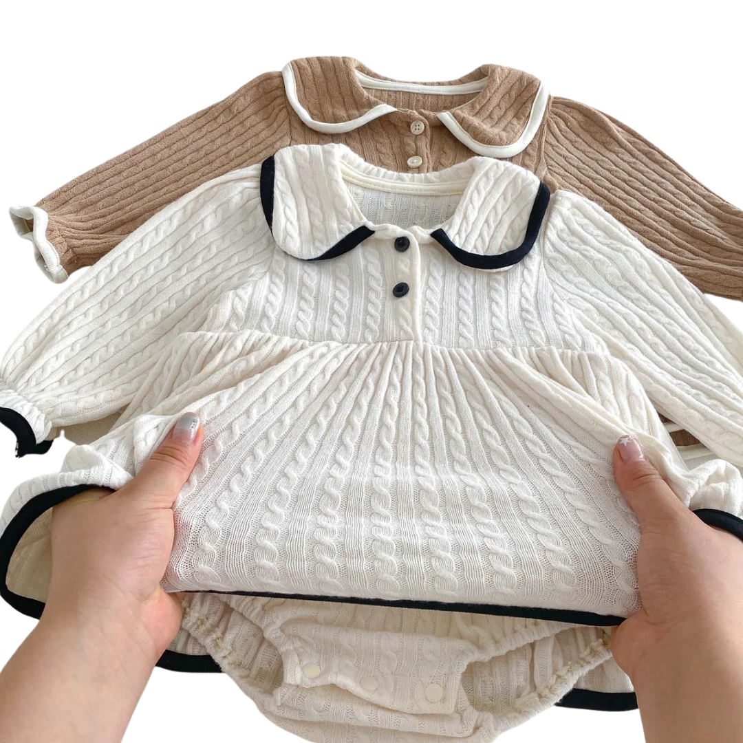 Hands lifting the skirt of the ivory cable knit dress to reveal the hidden built-in snap bodysuit underneath.