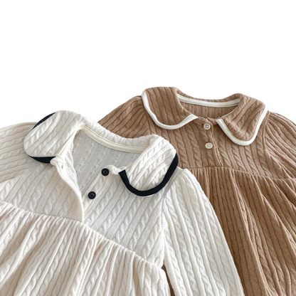Close up view of the contrasting dark Peter Pan collar and dual front buttons on the ivory baby girl knit dress.