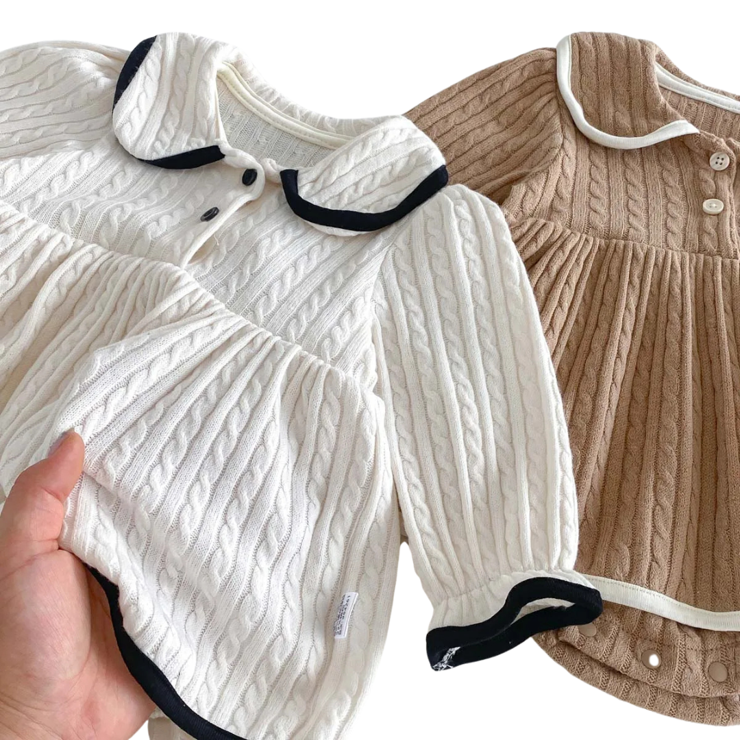 Hand gently pulling the skirt of the ivory baby dress to show the soft, stretchy nature of the premium knit fabric.
