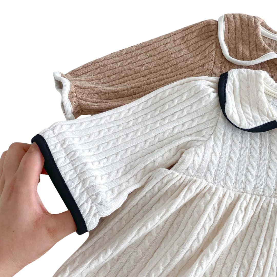 Hand holding the long sleeve of the ivory baby dress highlighting the cable knit texture and contrasting dark cuff trim.