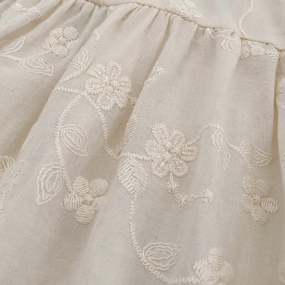 Close-up detail of delicate floral embroidery on ivory cotton blend fabric for girls special occasion dress.