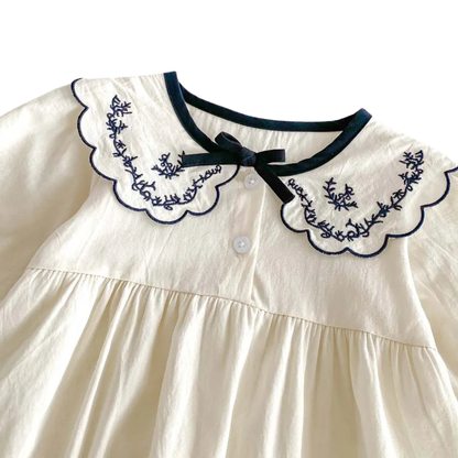 Flat lay of the ivory embroidered long sleeve bubble romper styled with cream baby shoes and dried floral accents.