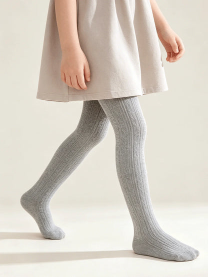 Little girl wearing light gray cable knit tights paired with a light-colored dress for fall.