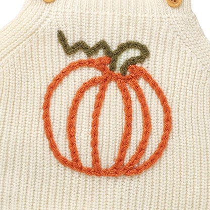 Close-up detail of the woven orange knit pumpkin graphic with a green stem on the cream baby romper.
