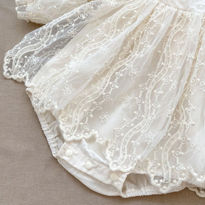 Close-up showing the layered mesh lace skirt and scalloped edges of an ivory baby bodysuit.