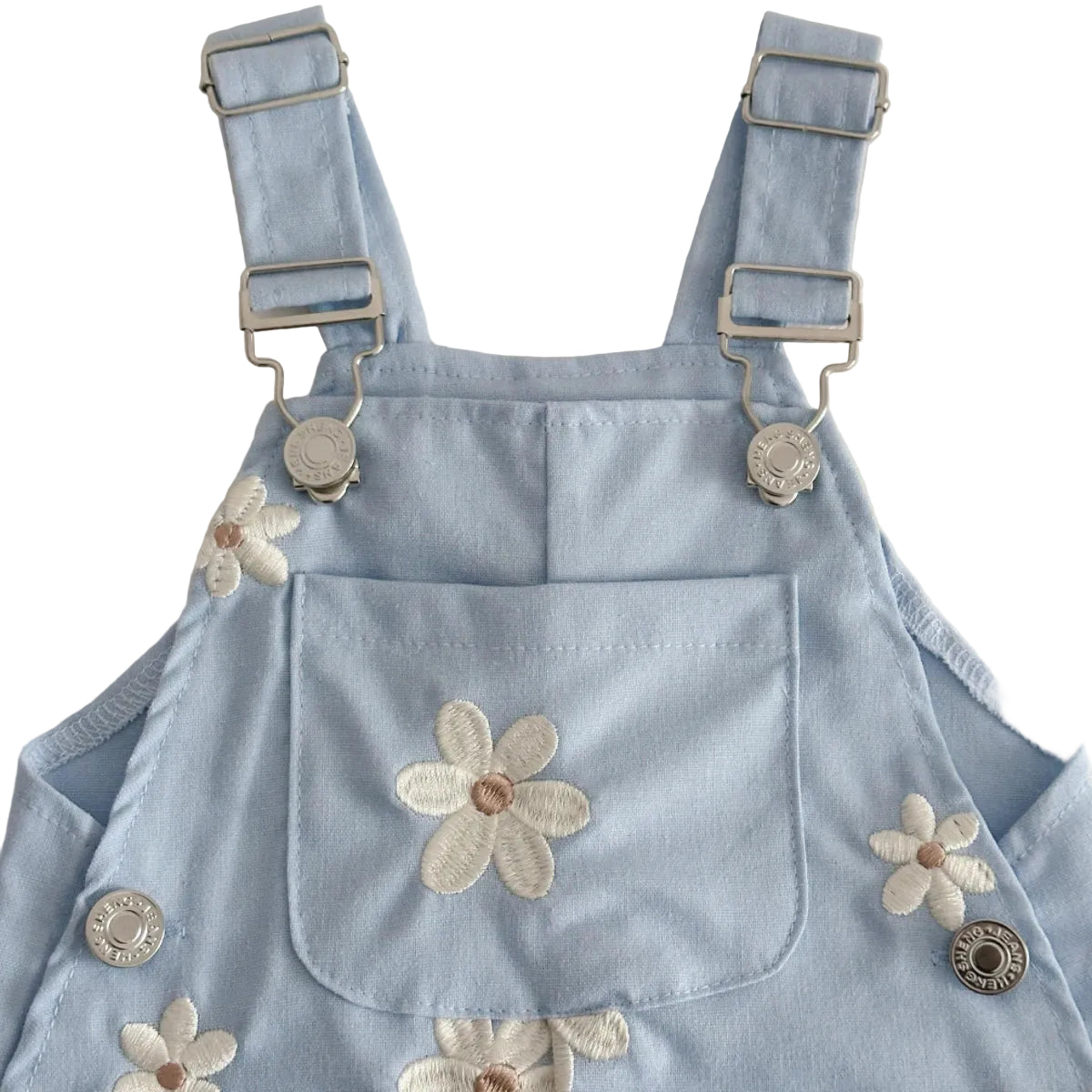 Close-up of the front bib pocket with a large embroidered daisy and adjustable metal buckle suspender straps on light blue baby overalls.