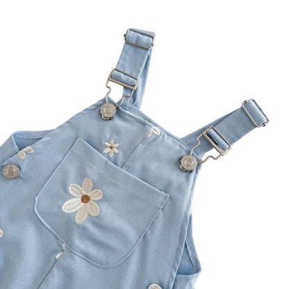Close-up side angle of light blue toddler overalls showcasing the metal side buttons, adjustable straps, and textured daisy embroidery.