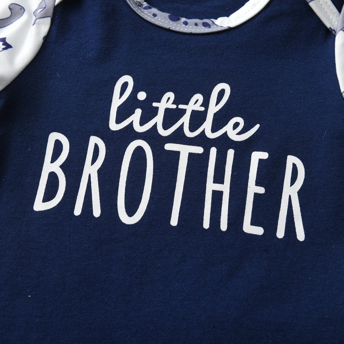 Extreme close-up of the white little BROTHER graphic text printed on the front of the navy blue baby bodysuit.