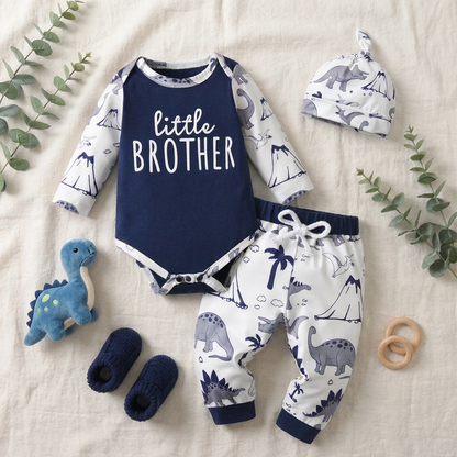 Styled flat lay of the little brother baby boy outfit on a textured cream blanket, arranged with a blue knit dinosaur toy, baby booties, and a wooden teething ring.