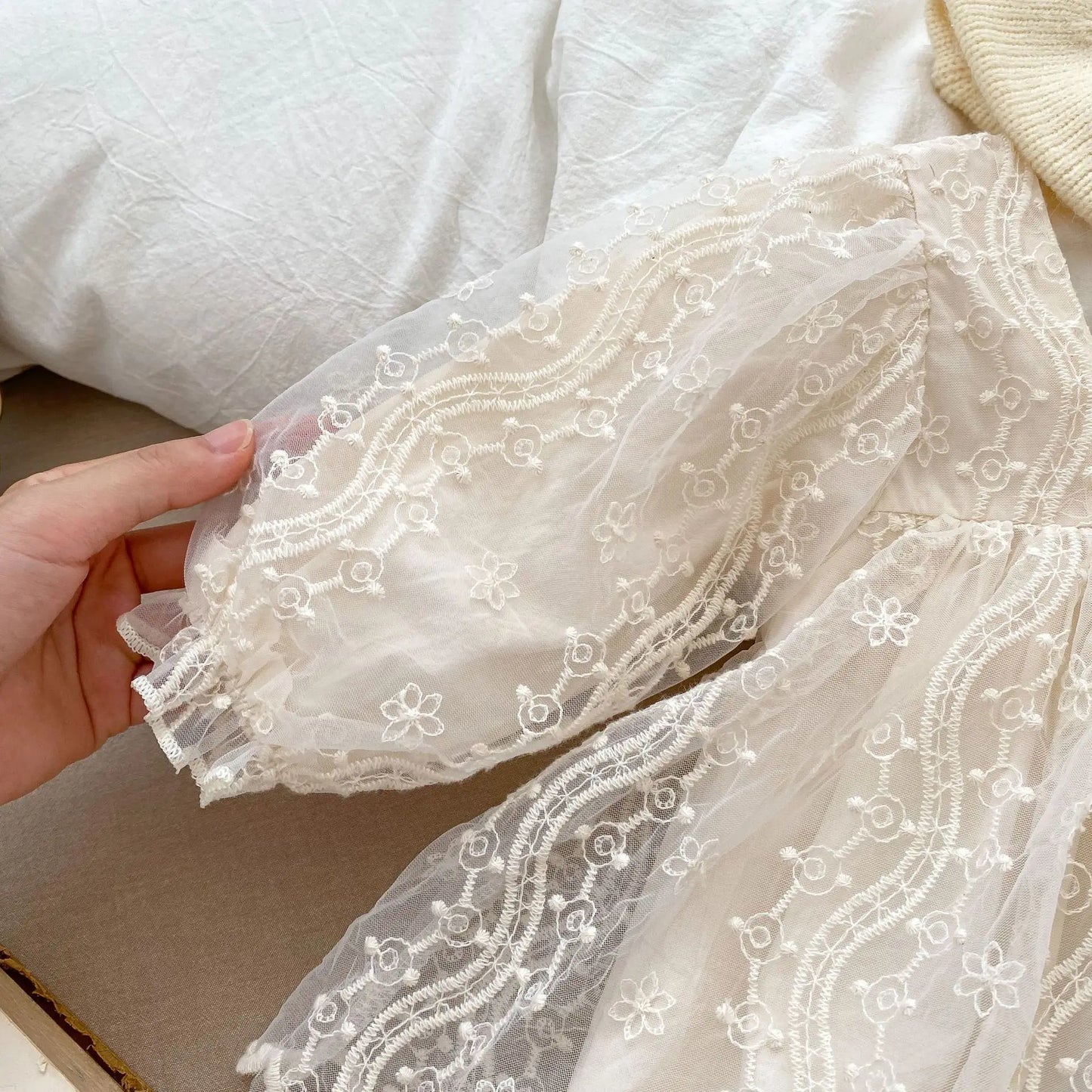 Close-up of the long puff sleeve on a cream baby lace romper, highlighting the delicate mesh and embroidery.