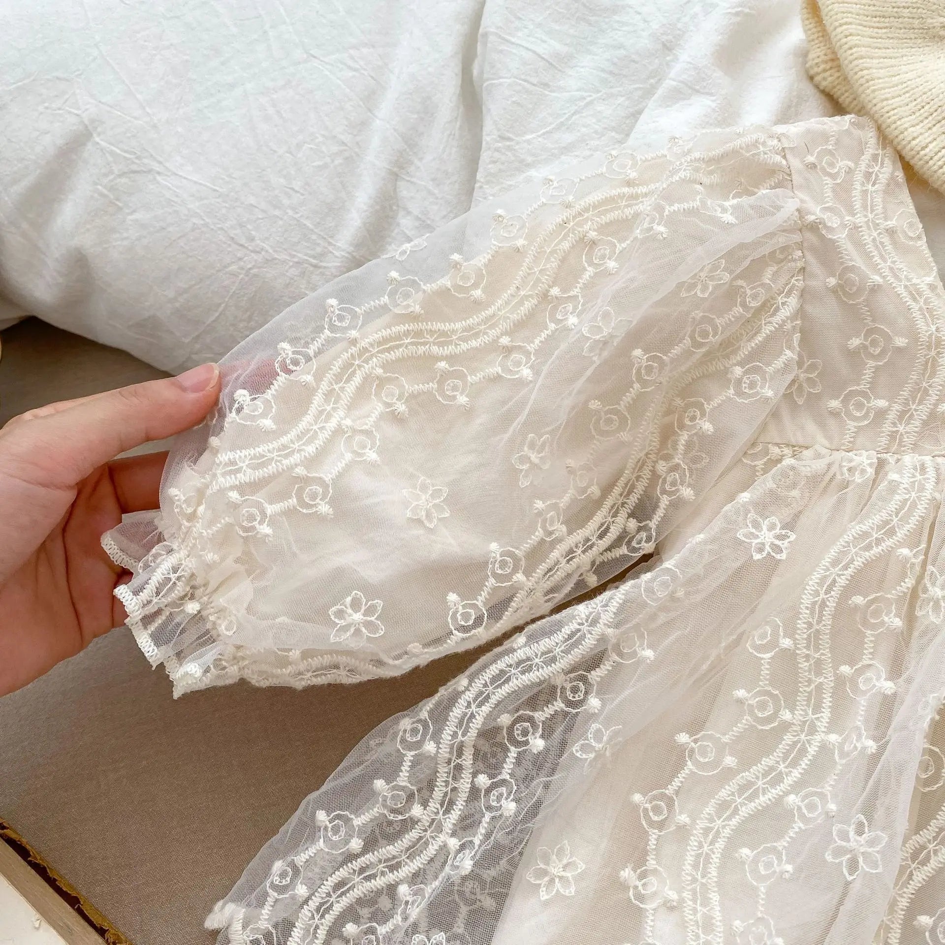 Close-up of the long puff sleeve on a cream baby lace romper, highlighting the delicate mesh and embroidery.